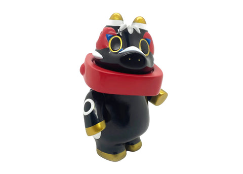 Akabegon- Black by Teresa Chiba is a black vinyl figure with gold accents, a red scarf, and wide yellow eyes. This stylized animal-like design stands upright and is considered a good luck charm.