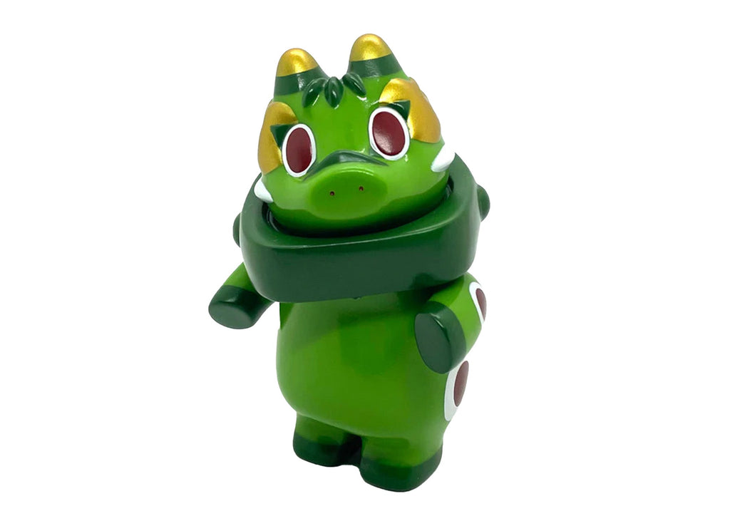 Akabegon- Green Tea by Teresa Chiba is a green, cartoon-style dragon figurine with red eyes, gold accents, and white spots. Standing upright against a white background, it serves as a whimsical good luck charm.