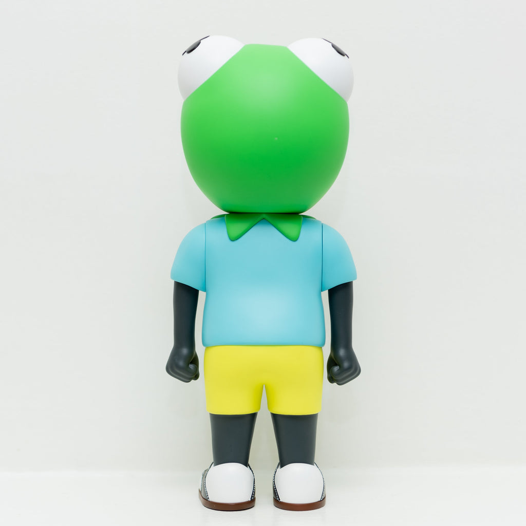 The limited edition Phibby — OG (Green) vinyl toy by Hebru Brand features a large green frog head, blue shirt, and yellow shorts, standing with its back to the camera against a plain white background.