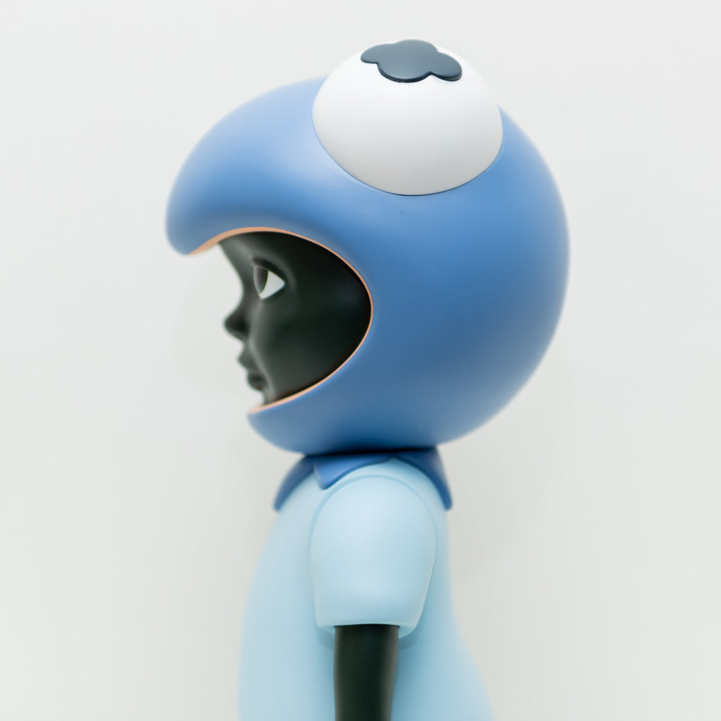 A side view of the limited edition Phibby — Purple vinyl figure by Hebru Brand, with dark skin, a large blue helmet featuring an eye, and a blue shirt, inspired by Hebru Brantley’s style against a plain white background.