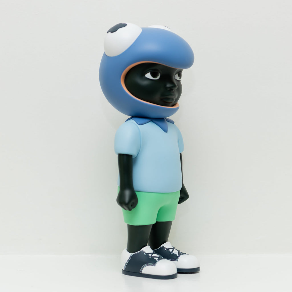 Phibby — Purple is a limited edition vinyl figure by Hebru Brand, featuring a child with dark skin in a large cartoon frog helmet, light blue shirt, green shorts, and white sneakers, inspired by Hebru Brantley’s signature style.