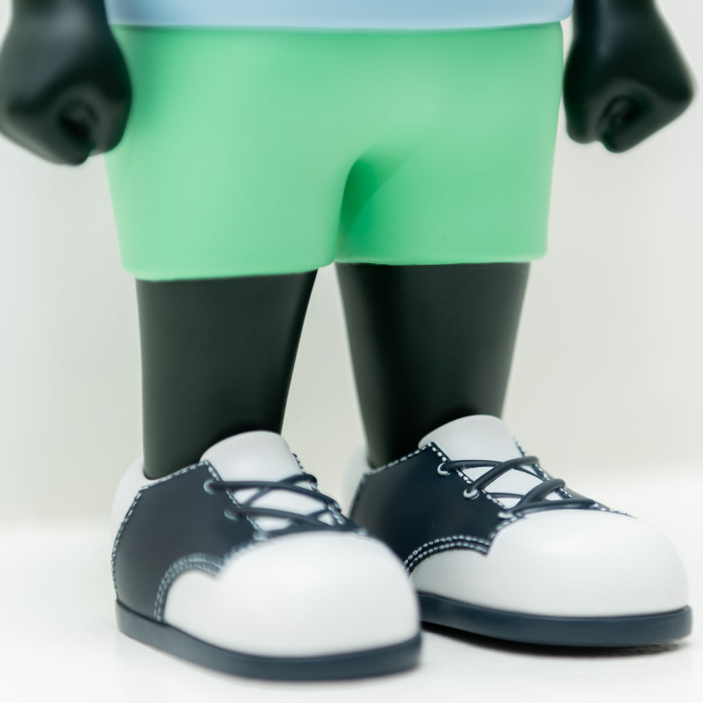 A close-up of the Hebru Brand Phibby — Purple limited edition vinyl figure, featuring light green shorts and black-and-white sneakers, standing on a white surface.