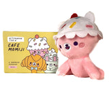 A cute plush with a cupcake hat sits next to a yellow Momiji Cafe Momiji Blind Box, featuring cartoon dessert characters from the