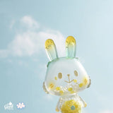 Lemon Soda Robin by A Good Company—a translucent bunny figure with yellow and green accents—stands out against a blue sky with scattered clouds, making it a perfect shelf ornament for charming home decor. Logos are in the lower-left corner.
