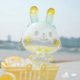 The Lemon Soda Robin by A Good Company is a translucent figurine with yellow-tipped ears, sitting in a yellow cart filled with ice cubes and lemon slices—an ideal home decor piece to brighten up your shelves.