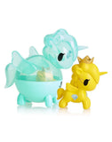 Two small tokidoki Unicorno Capsule Cuties Blind Box figures—one transparent blue with wings and one solid yellow with a crown and diamond—are displayed side by side on a white background.