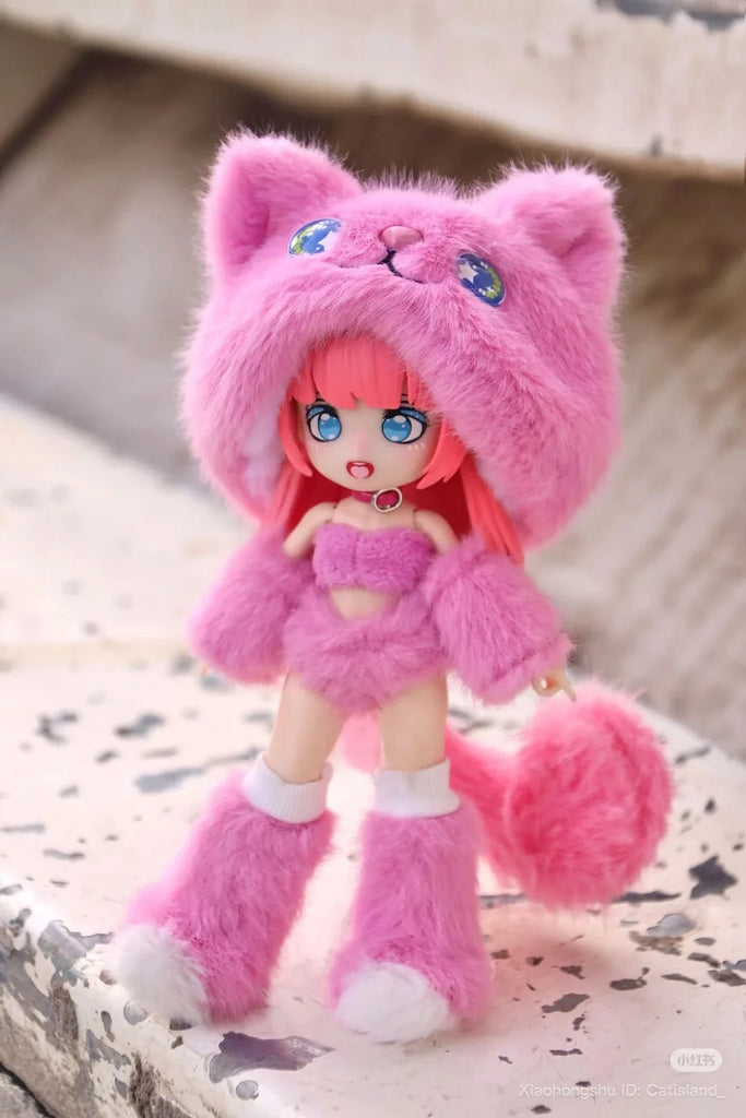A ball-jointed doll with pink hair in a fluffy pink cat costume, including ears, mittens, boots, and tail, stands on a weathered stone. This adorable figure is from the BIJIDI Cat Island — Black Cat Or Candy Cat? blind box collection.