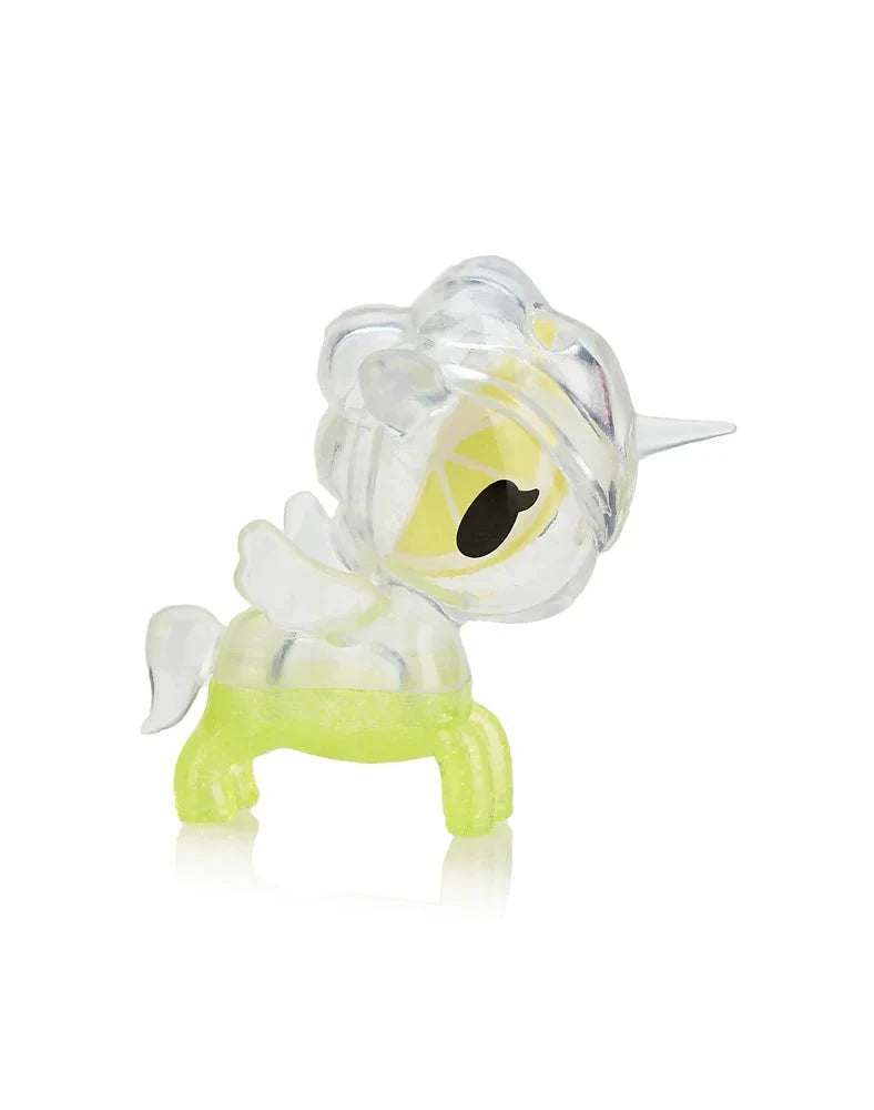 A small, translucent plastic unicorn figurine by tokidoki, inspired by the Toki Mochi Donut Unicorno Blind Bag, featuring a yellow body, white mane and tail, and a clear horn, shown in profile.
