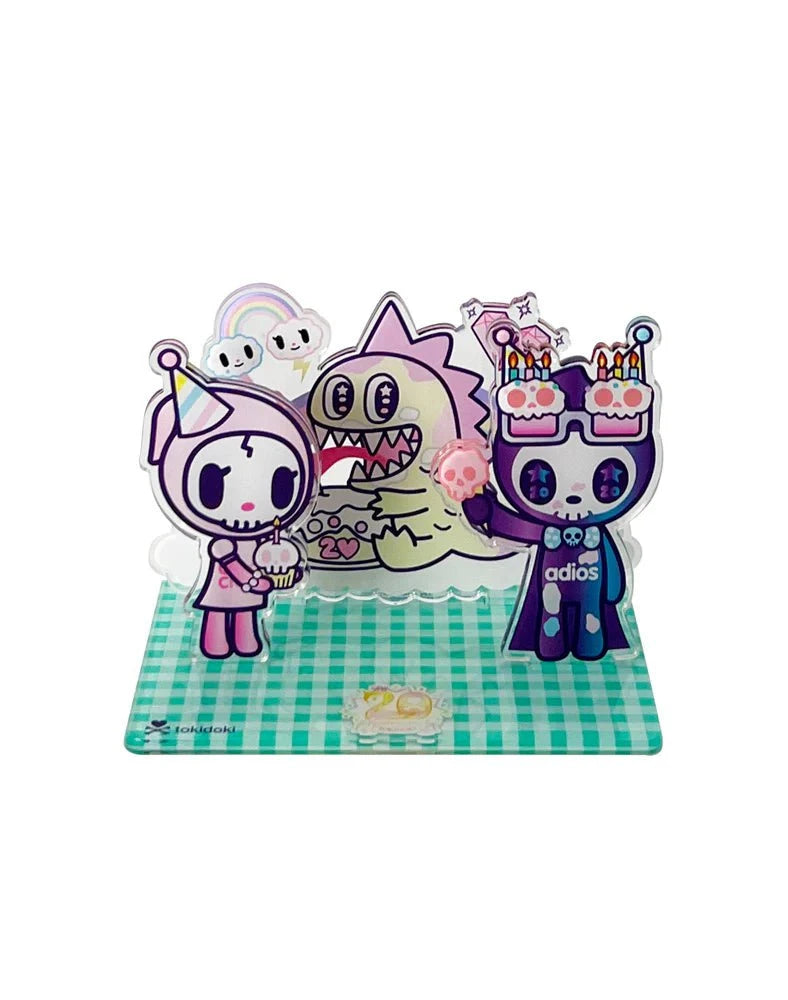Three cartoon characters, including a skeleton and a creature in a birthday hat, celebrate tokidoki’s 20th Anniversary on a green checkered base with cakes and candles in this cute Tokidoki 20th Anniversary Acrylic Standee Blind Box collectible.