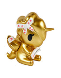 The tokidoki Fortune Cookie Unicorno Blind Box features a gold figurine with a bandaged horn and wing, holding a white fortune slip reading