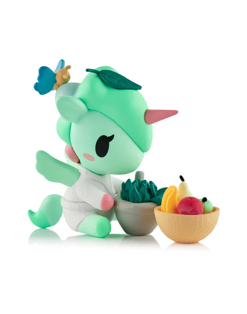 A pastel green Spa Day Unicorno Blind Box figurine by tokidoki sits among fruit and veggie bowls on a white background, adding kawaii wellness vibes to your space.