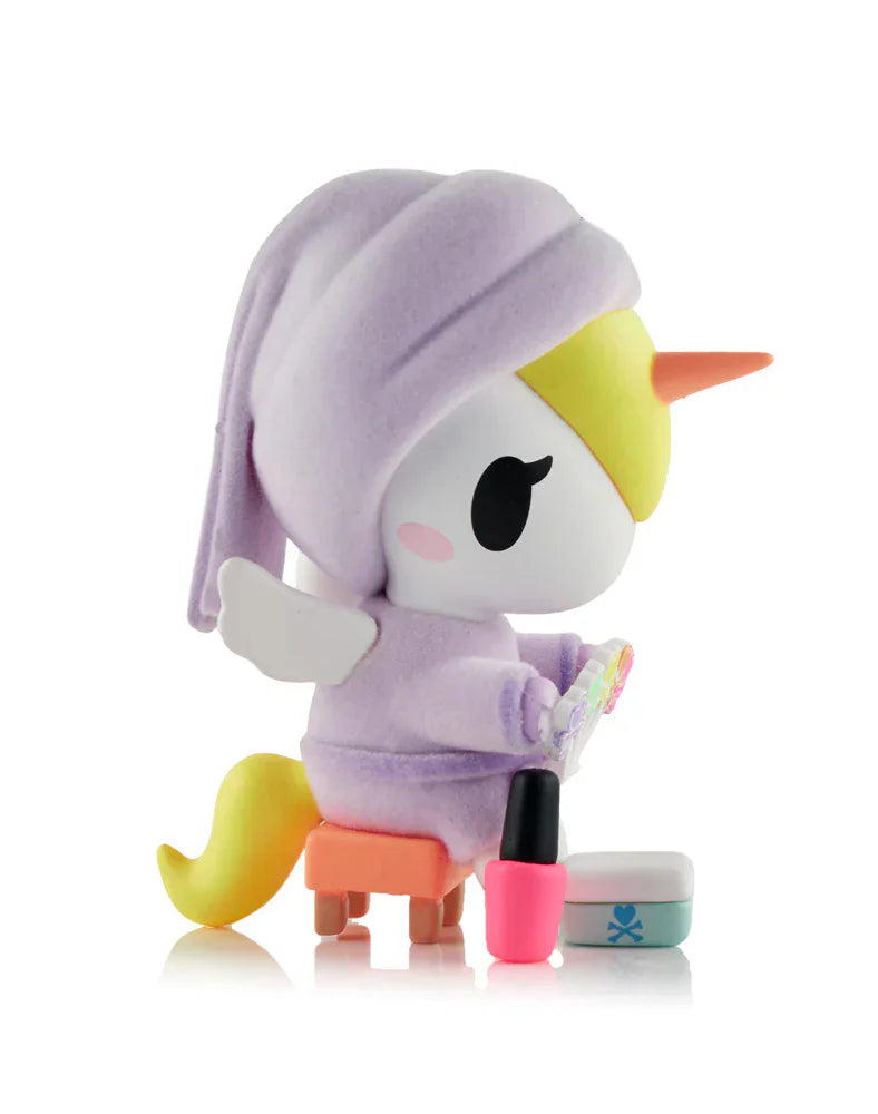 The tokidoki Spa Day Unicorno Blind Box features a Unicorno in a purple robe and head wrap, yellow mane, orange horn, and wings, sitting on a stool with mirror and nail polish—ideal for kawaii collectors.