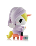 The tokidoki Spa Day Unicorno Blind Box features a Unicorno in a purple robe and head wrap, yellow mane, orange horn, and wings, sitting on a stool with mirror and nail polish—ideal for kawaii collectors.