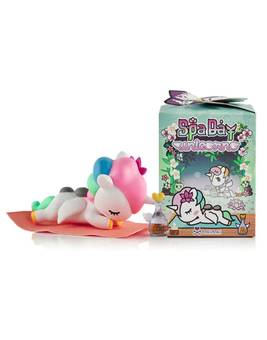 A small tokidoki unicorn figurine with a towel and eye mask rests on a mat beside the Spa Day Unicorno Blind Box, capturing kawaii wellness in this adorable collectible.