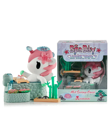 The Spa Day Unicorno - Hot Spring Oasis (Special Edition) by tokidoki relaxes in a hot spring, adorned with a flower headpiece and peaceful spa vibes, displayed beside its packaging.