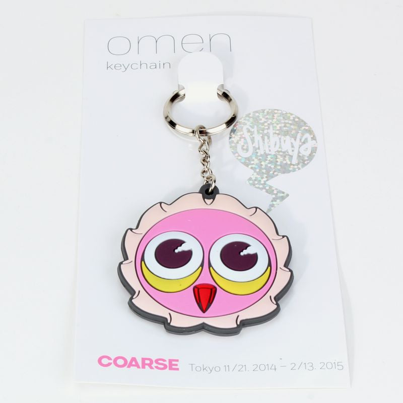 The Omen Shibuya Keychain by Coarse features a cartoon pink owl face with large eyes, attached to a card labeled