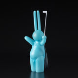 The Daily Flasher by mr. clement from Tomenosuke Shoten is a blue, glow-in-the-dark vinyl rabbit figurine standing upright with a white selfie stick in one hand, displayed against a black background.