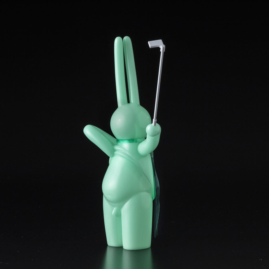 The Daily Flasher by mr. clement from Tomenosuke Shoten is a mint green, glow-in-the-dark vinyl toy rabbit holding a selfie stick, shown facing away against a black background.
