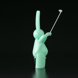 The Daily Flasher by mr. clement—a mint-green, glow-in-the-dark vinyl rabbit toy from Tomenosuke Shoten—stands upright holding a selfie stick, making it a playful collectible against a black background.