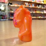 The Pop Soda Popsoda Finger Puppet - Orange, an abstract orange and pink plastic figurine, stands upright on a wooden surface with shelves of colorful items blurred in the background.