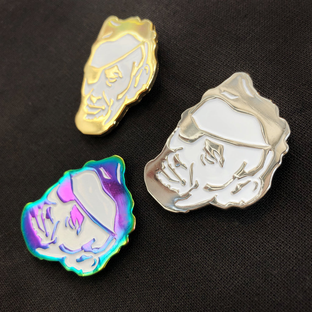 Three Rotofugi Pirate Abe Enamel Pins—head with eyepatch designs in gold, silver, and iridescent finishes—are displayed on black fabric. A unique accessory by Rotofugi for designer toy fans.