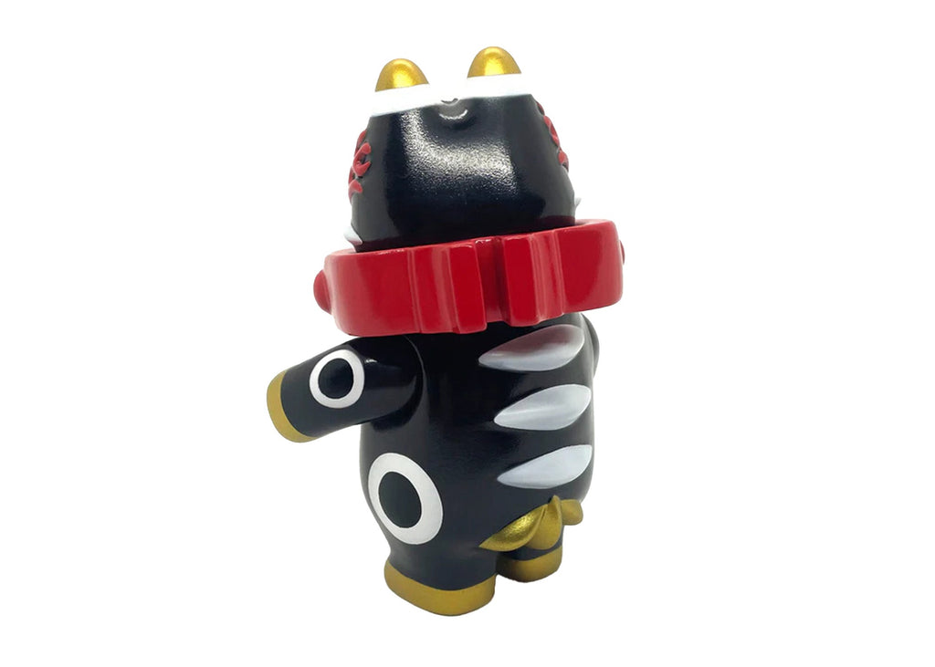 The Akabegon-Black vinyl figurine by Teresa Chiba features a stylized black cat with gold ears, white fangs, circular eye patterns, and a red collar, standing with a raised arm—a unique good luck charm.