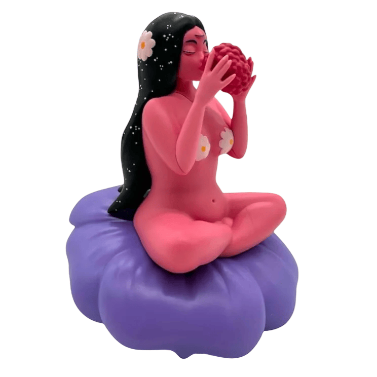 Flower Girl by UVD Toys is a stylized pink collectible figure with black hair, floral designs, and a red object, sitting cross-legged on a purple cushion—a unique gift perfect for any collector.