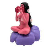 Flower Girl by UVD Toys is a unique pink figure with long black hair, sitting cross-legged on a purple cushion and holding a red object—a collectible adorned with flowers and the perfect gift for collectors.