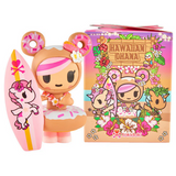 A kawaii donut-themed figurine with a pink surfboard stands by the tokidoki Hawaiian Ohana Blind Box, which features vibrant character art and floral designs—perfect for fans of tropical collectibles.