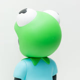 Phibby — OG (Green) by Hebru Brand is a limited edition vinyl featuring a green cartoon frog with big eyes and a blue shirt with a green collar, posed facing away against a plain white background. Inspired by Hebru Brantley.
