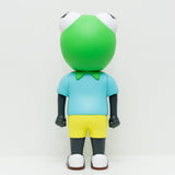 The limited edition Phibby — OG (Green) vinyl toy by Hebru Brand features a large green frog head, blue shirt, and yellow shorts, standing with its back to the camera against a plain white background.