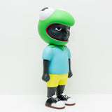 Phibby — OG (Green) by Hebru Brand is a limited edition vinyl figurine depicting a dark-skinned person in a large green frog head, light blue shirt, yellow shorts, and black shoes, styled uniquely by Hebru Brantley against a white background.