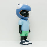Phibby — Purple is a limited edition vinyl figure by Hebru Brand, featuring a child with dark skin in a large cartoon frog helmet, light blue shirt, green shorts, and white sneakers, inspired by Hebru Brantley’s signature style.