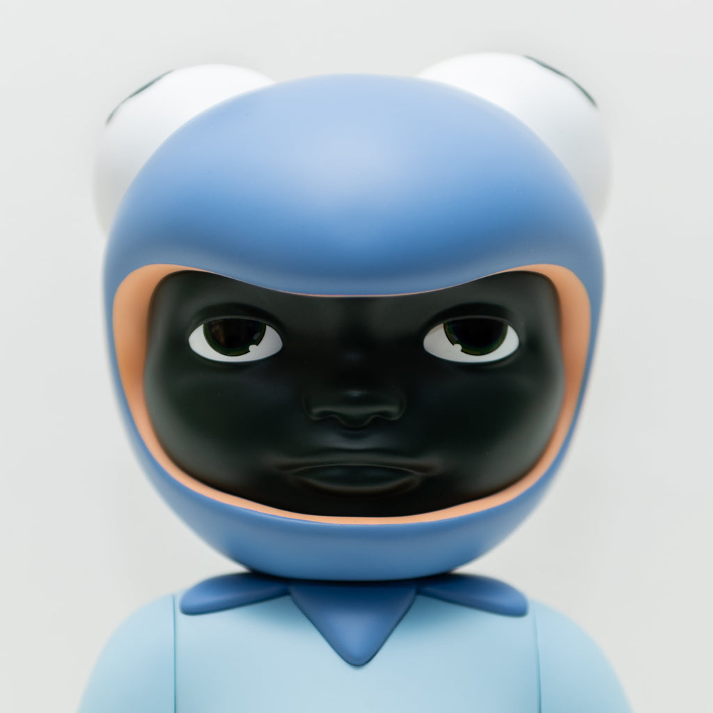 Phibby — Purple by Hebru Brand is a limited edition vinyl figure with a stylized dark face, blue outfit, and a hood shaped like a frog’s head with large eyes, inspired by Hebru Brantley’s signature style.