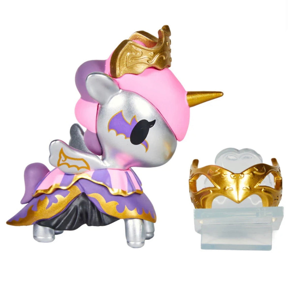 A silver Unicorno After Dark Masquerade Blind Box collectible toy by tokidoki, with a pink mane and purple-gold outfit and crown, stands beside a gold and purple mask accessory on a clear stand.