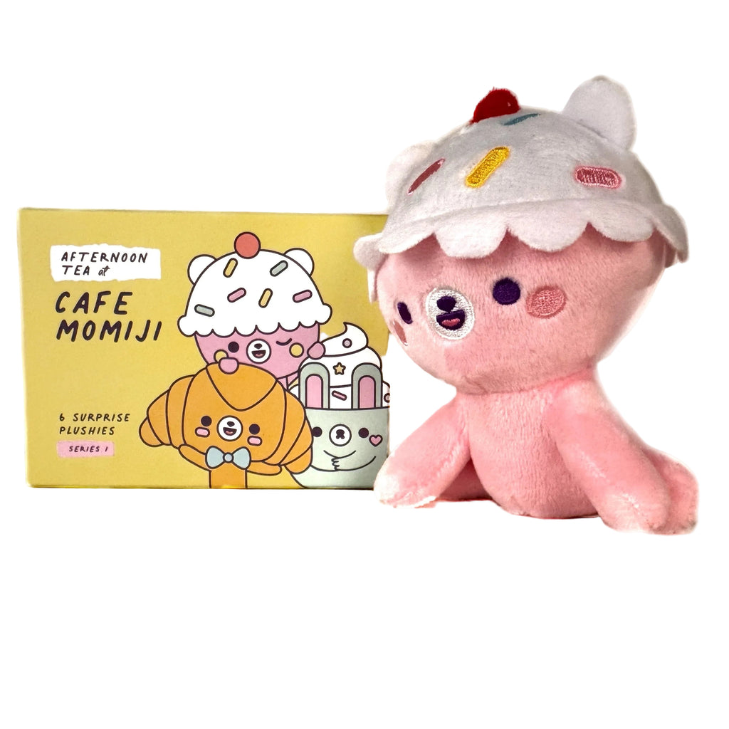 A cute plush with a cupcake hat sits next to a yellow Momiji Cafe Momiji Blind Box, featuring cartoon dessert characters from the 
