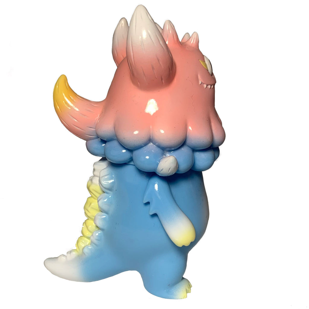 The Little Hut’s Rangeas Jr. - Light Blue/Pink features a pastel monster with a pink head, large horns, blue body, and yellow-tipped tail—an adorable collectible standing upright on a white background.