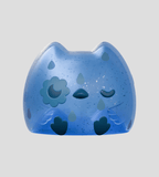 Kairos the Owl Blind Box by Kaleidos Creative features a blue, owl-shaped figure with closed eyes, floral detail on its left cheek, small dark blue paw prints, and a plain light gray background.