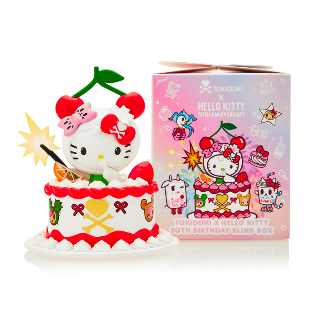 A Hello Kitty figurine with cherries on its head sits in a decorative cake beside a pink tokidoki Tokidoki x Hello Kitty 50th Birthday Blind Box.