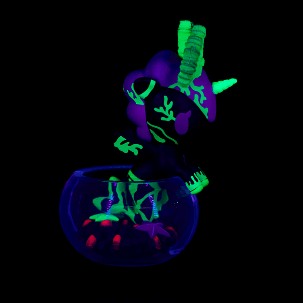 The tokidoki Neon Reef Mermicorno - Deep Star Coral Special Edition features glow-in-the-dark neon green and purple patterns inside a translucent bowl, shining brightly under blacklight against a dark backdrop.