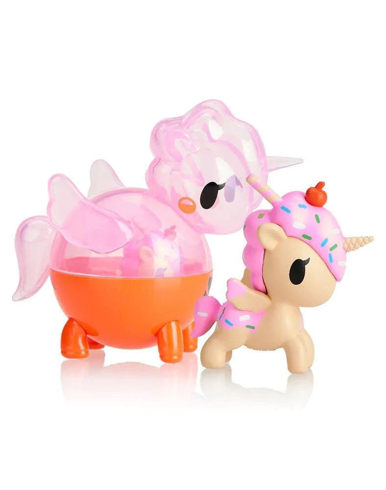 Two small, colorful toy figures: a translucent pink and orange winged creature and a tokidoki Unicorno with cupcake-themed design and sprinkles from the Unicorno Capsule Cuties Blind Box series.