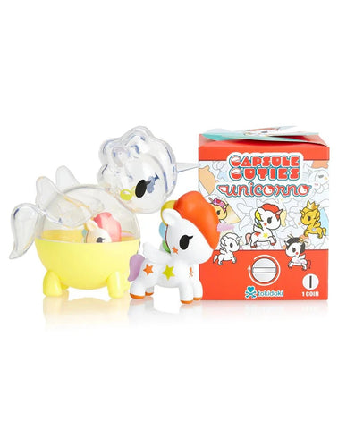 A unicorn figurine with a red mane and orange tail stands next to a yellow capsule and the red tokidoki Unicorno Capsule Cuties Blind Box decorated with cartoon unicorns.