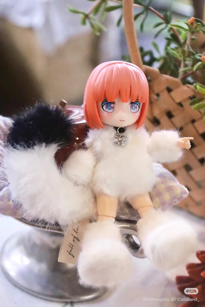 A BIJIDI Cat Island — Black Cat Or Candy Cat? Blind Box ball-jointed doll with pink hair and a fluffy white outfit sits on a cushion beside a decorative plant basket.