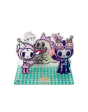 Three cartoon characters, including a skeleton and a creature in a birthday hat, celebrate tokidoki’s 20th Anniversary on a green checkered base with cakes and candles in this cute Tokidoki 20th Anniversary Acrylic Standee Blind Box collectible.