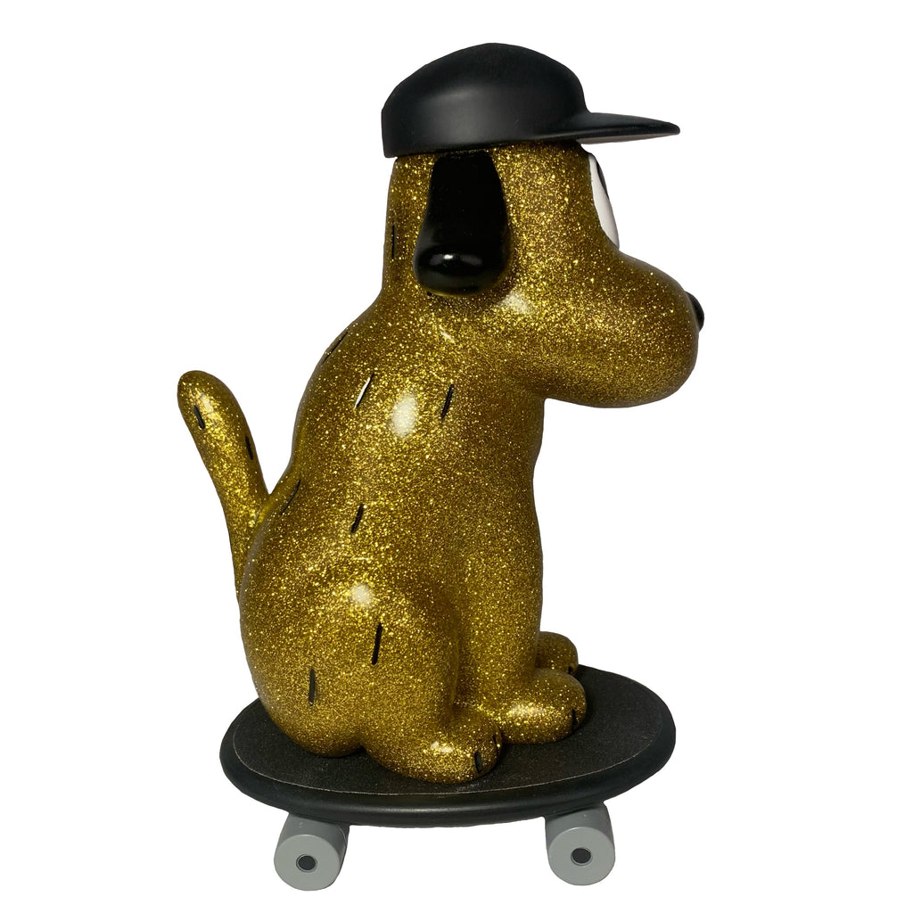 The How2Work One Chu Sk8- Gold figure, featuring gold glitter and a black cap, is posed on a skateboard and photographed from the side against a white background.