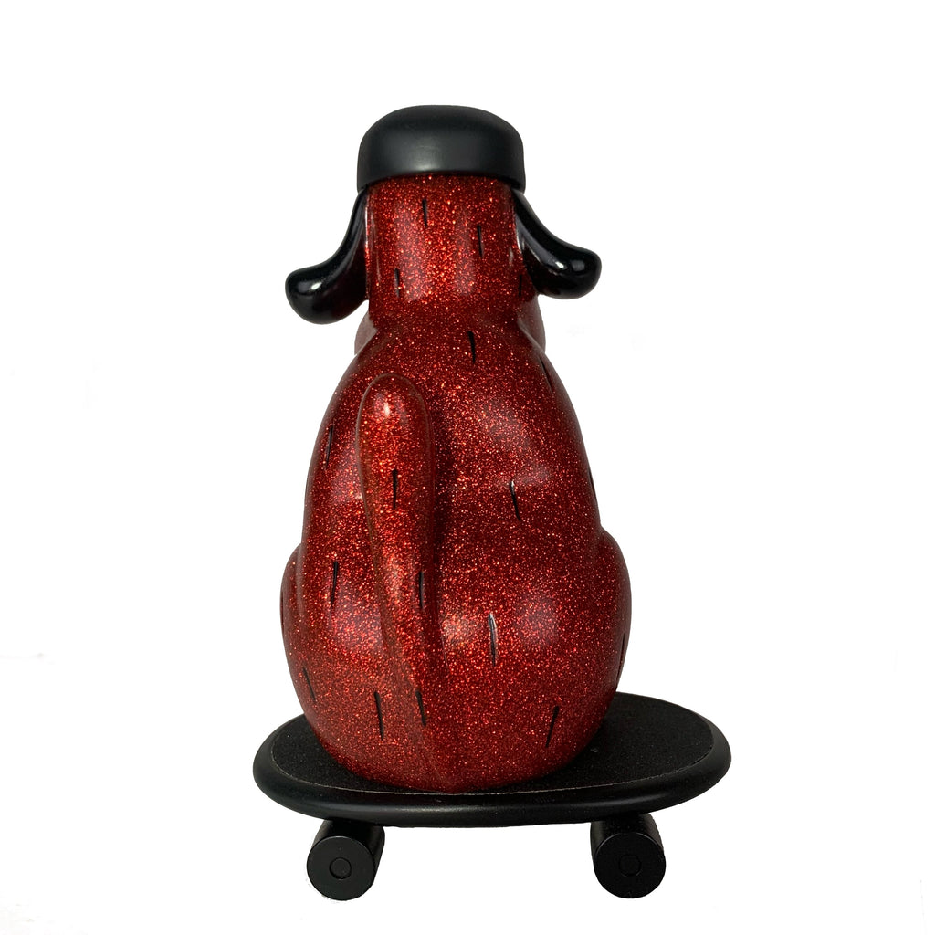 The How2Work One-Chu Sk8 - Red Glitter is an 8-inch collectible figure with a black cap, sitting on a round black base with four wheels, viewed from the back and resembling a red glitter skateboard.