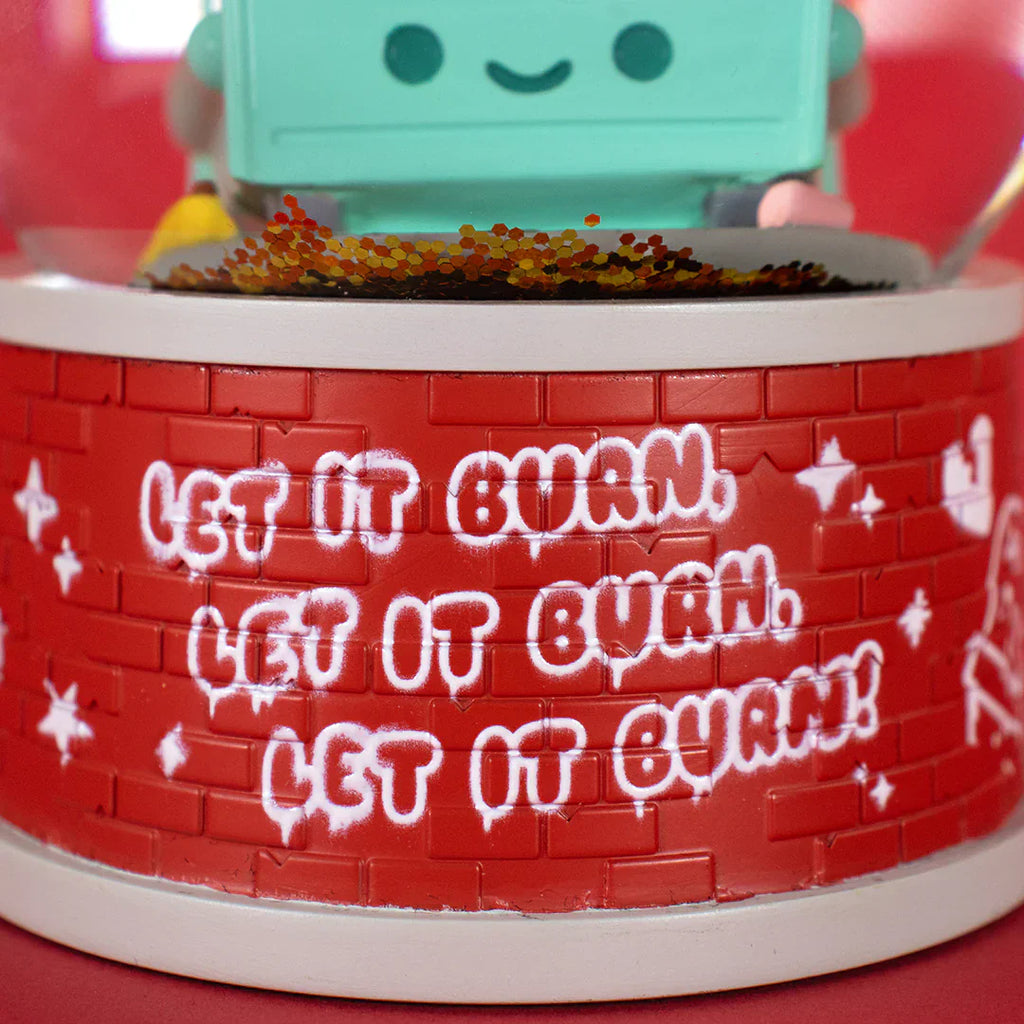 A close-up of 100% Soft’s Dumpster Fire Snow Globe features red with graffiti-style 