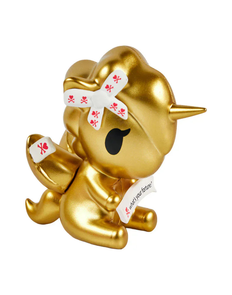 The tokidoki Fortune Cookie Unicorno Blind Box features a gold figurine with a bandaged horn and wing, holding a white fortune slip reading 