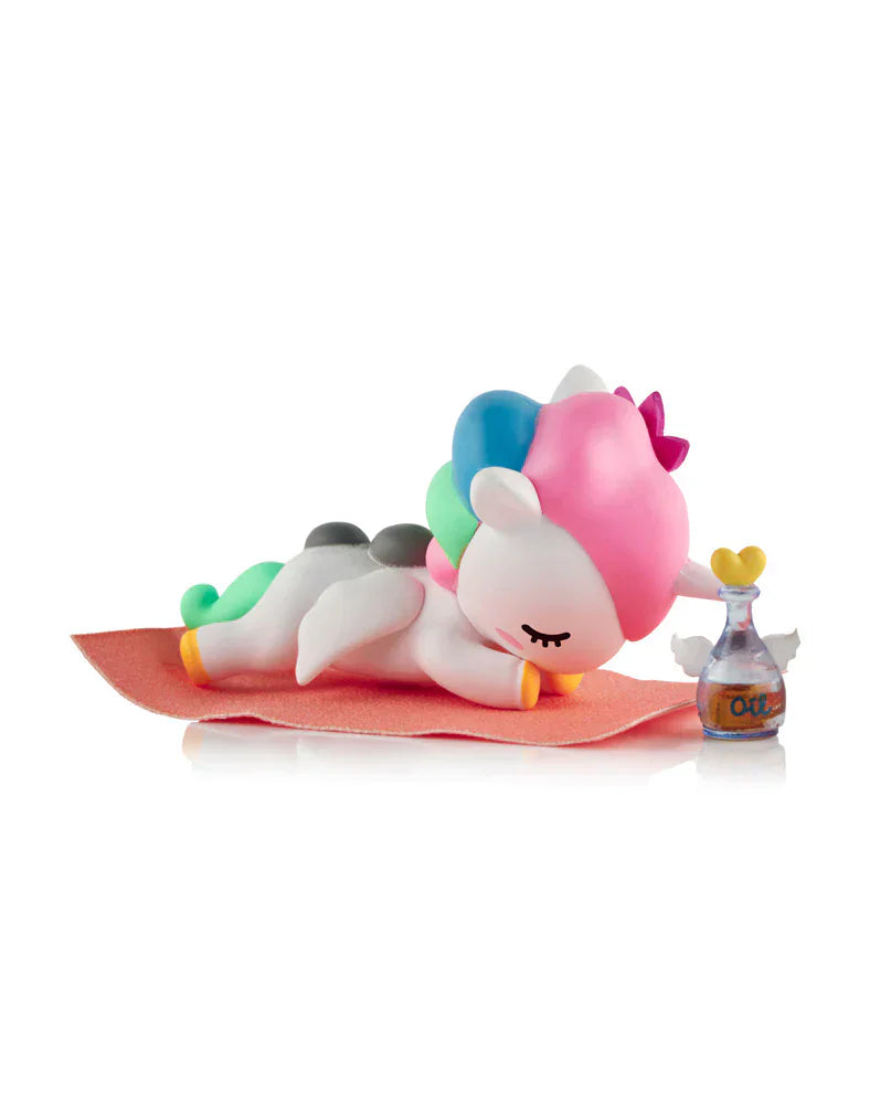 The tokidoki Spa Day Unicorno Blind Box features a cute Unicorno figurine with a colorful mane, face-down on a pink mat beside a small bottle with a yellow heart cap—perfect for adding kawaii wellness vibes to your space.