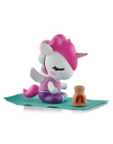 The Spa Day Unicorno Blind Box by tokidoki features a cute figurine with pink hair, cross-legged on a teal mat beside a tiny brown fireplace—a kawaii wellness scene ideal for any blind box collector.